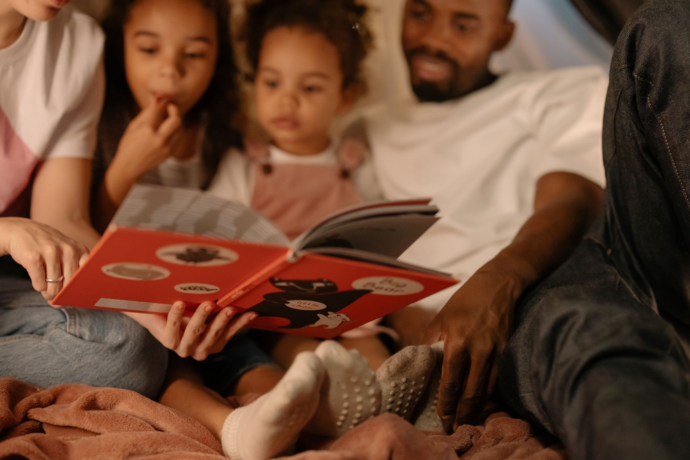 Parents and children reading together in a warmly lit blanket fort.