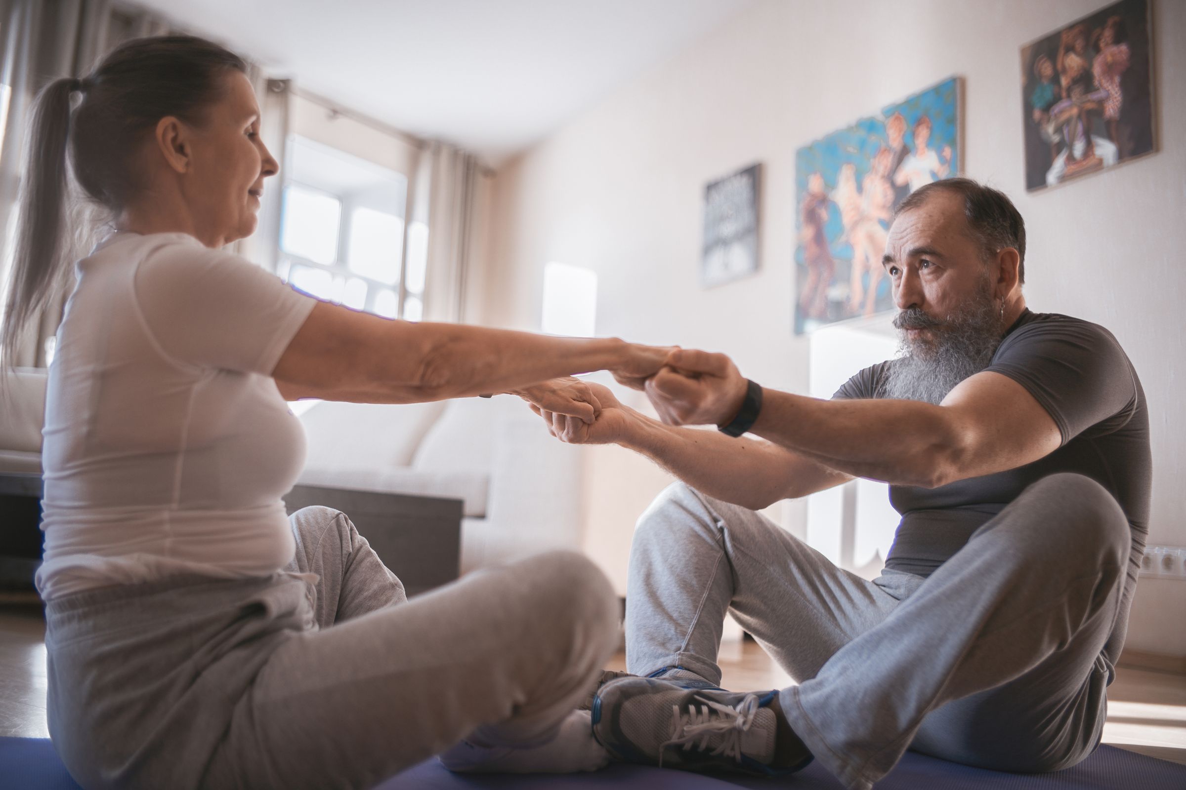 An older couple stretching together in their living room.