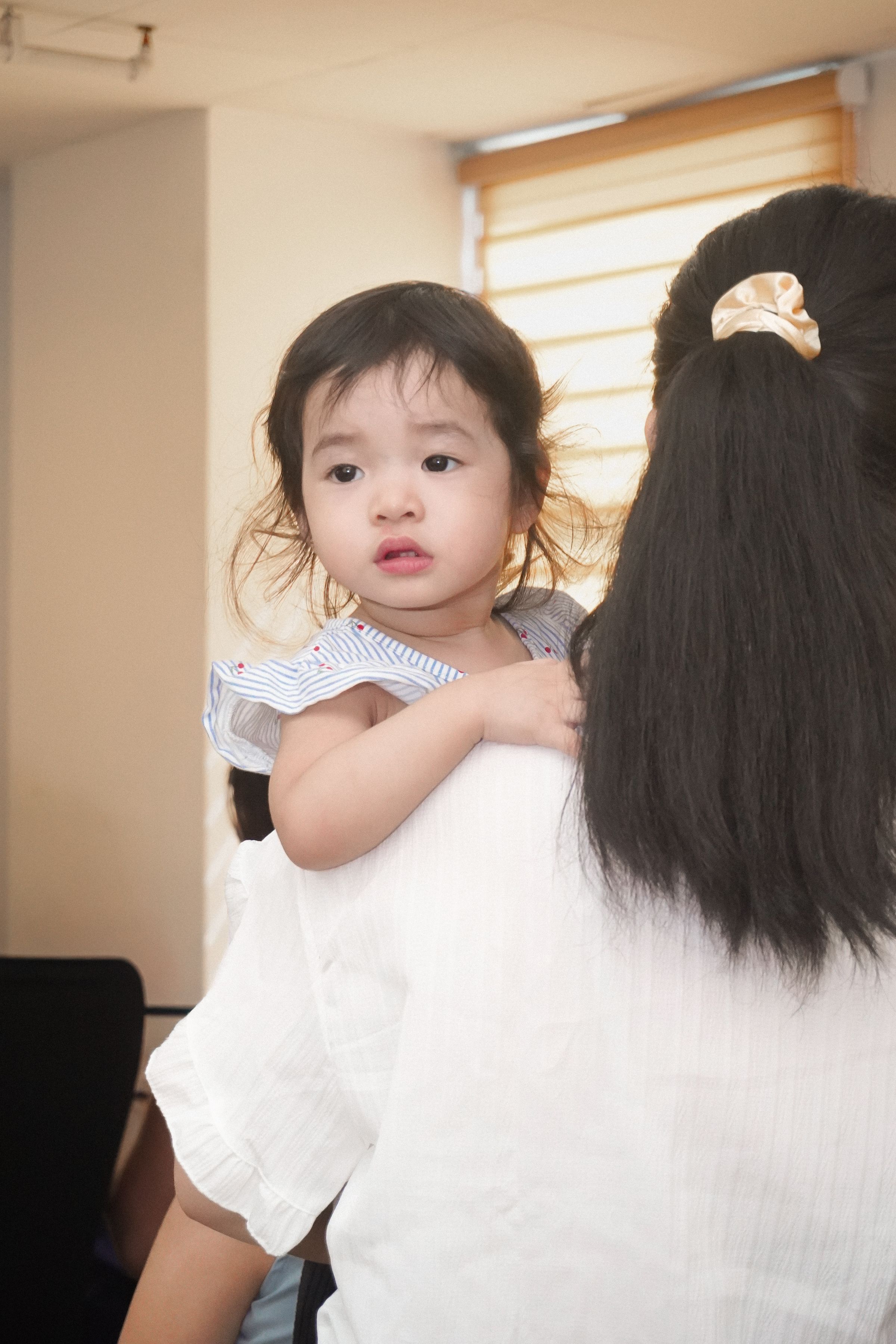 A parent holding a young child in soft light at home.