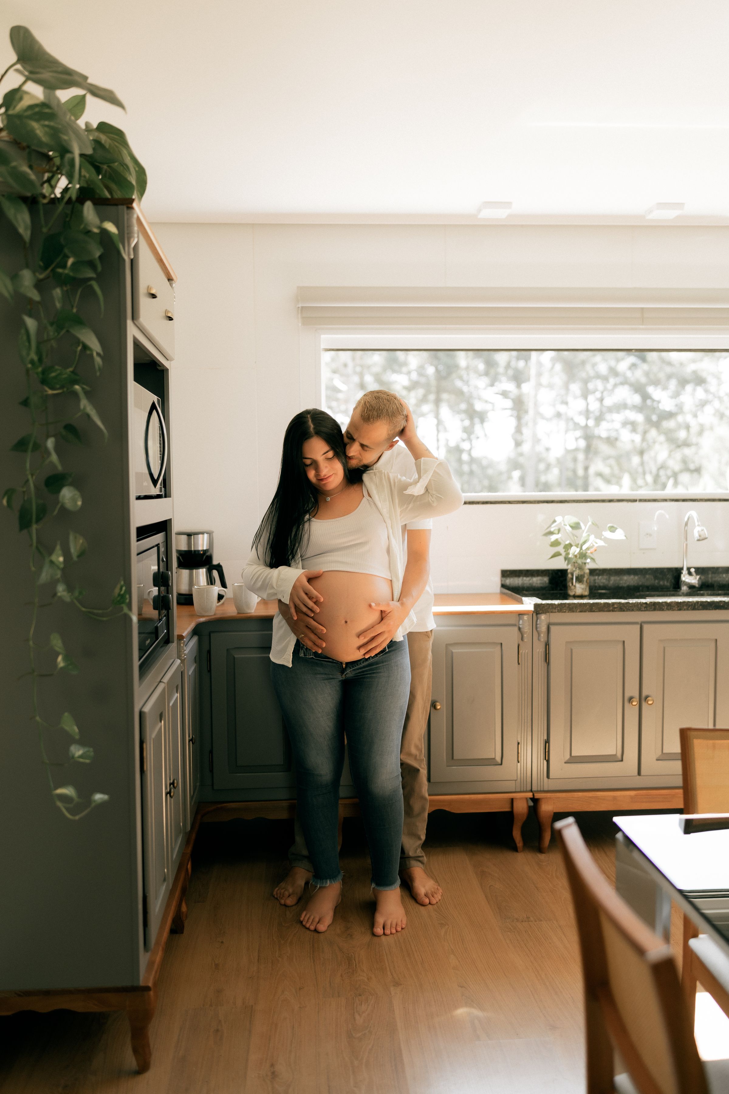 A couple embracing in a sunlit kitchen while expecting a child.